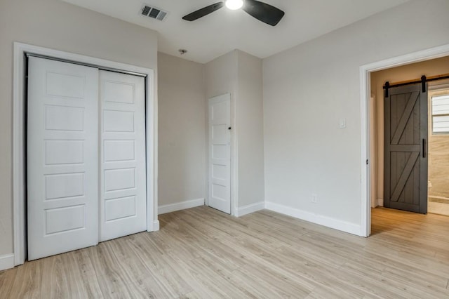 unfurnished bedroom with ceiling fan, a barn door, light hardwood / wood-style floors, and a closet