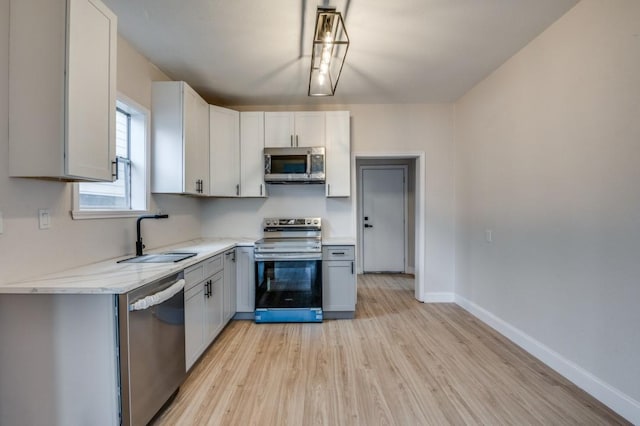 kitchen with white cabinetry, sink, stainless steel appliances, light stone countertops, and light hardwood / wood-style flooring