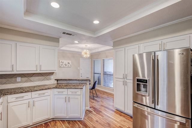 kitchen featuring dark stone counters, a raised ceiling, white cabinets, and stainless steel refrigerator with ice dispenser