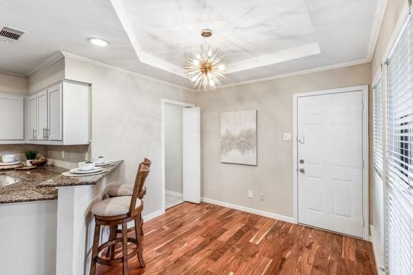 kitchen with dark stone counters, decorative light fixtures, a raised ceiling, and hardwood / wood-style floors