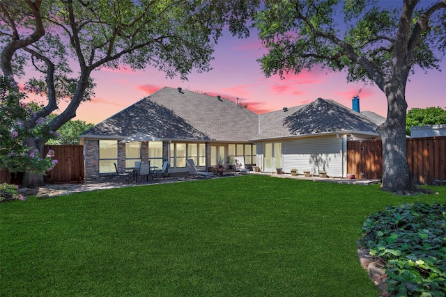 back house at dusk featuring a yard and a patio