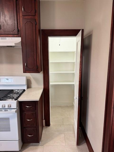 kitchen featuring dark brown cabinetry, white gas range, and light tile patterned floors