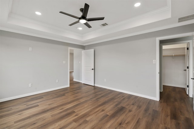 unfurnished bedroom with dark hardwood / wood-style floors, ornamental molding, a walk in closet, ceiling fan, and a raised ceiling