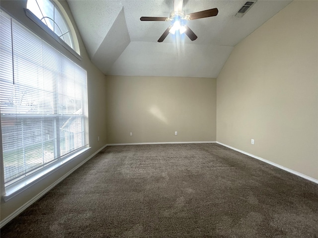 spare room with ceiling fan, vaulted ceiling, a textured ceiling, and dark colored carpet