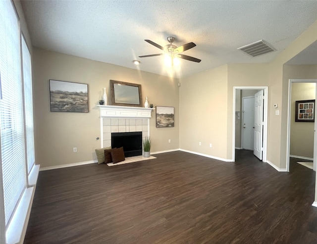 unfurnished living room with dark wood-type flooring, ceiling fan, a tiled fireplace, and a textured ceiling