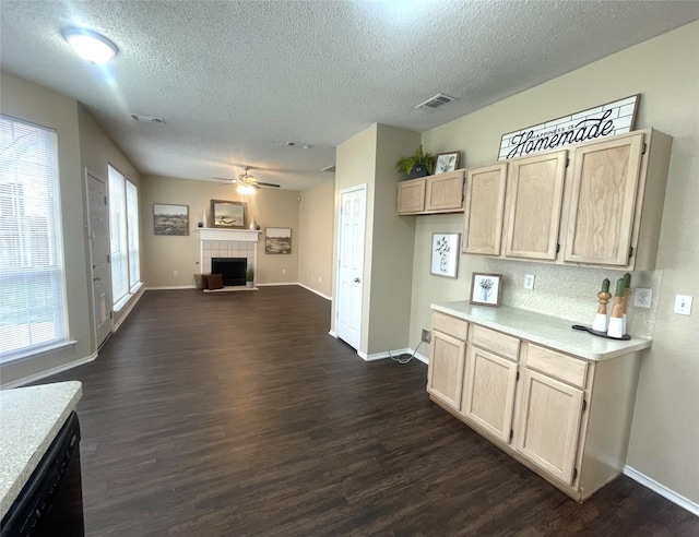 kitchen with dark wood-type flooring, light brown cabinetry, black dishwasher, ceiling fan, and a tiled fireplace