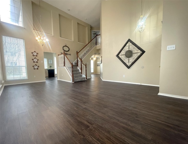 unfurnished living room with an inviting chandelier, a towering ceiling, and dark wood-type flooring