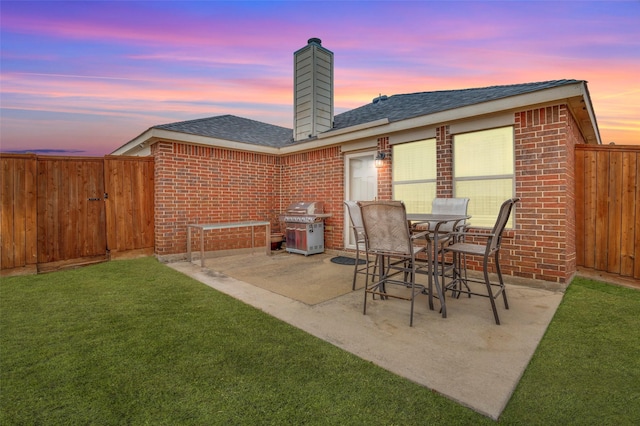 patio terrace at dusk featuring area for grilling and a lawn