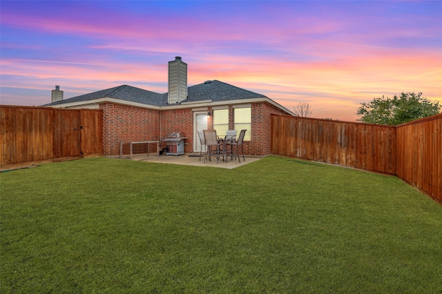 back house at dusk featuring a yard and a patio area