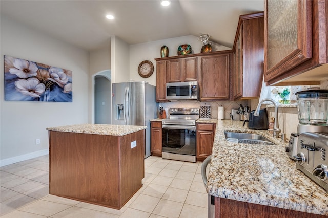 kitchen with light tile patterned flooring, sink, light stone counters, a kitchen island, and stainless steel appliances