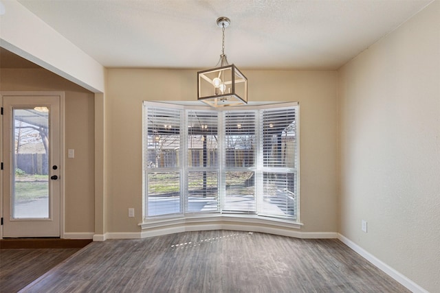 unfurnished dining area with dark wood-type flooring, a chandelier, and plenty of natural light