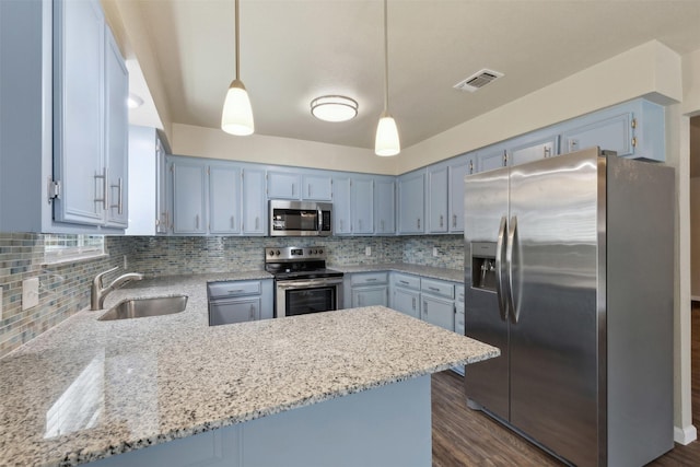 kitchen with sink, appliances with stainless steel finishes, light stone counters, decorative light fixtures, and kitchen peninsula