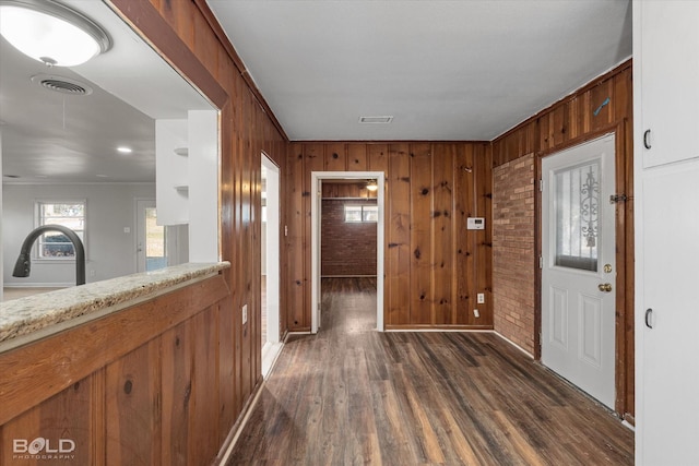 hallway featuring a sink, wooden walls, visible vents, and dark wood-style flooring