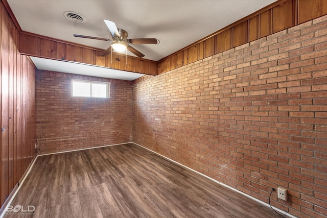 spare room featuring ceiling fan, brick wall, visible vents, and dark wood finished floors