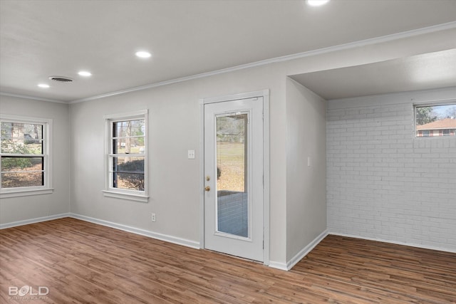 doorway featuring baseboards, brick wall, ornamental molding, and wood finished floors