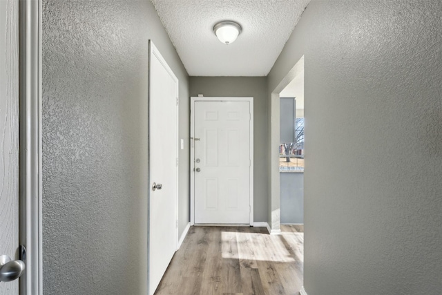 hall featuring light wood-type flooring and a textured ceiling