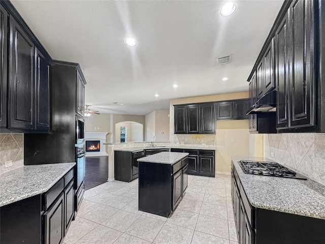 kitchen with gas cooktop, backsplash, a center island, light stone countertops, and light tile patterned flooring