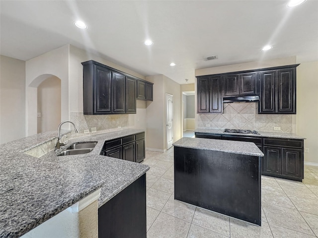 kitchen featuring sink, light stone countertops, decorative backsplash, kitchen peninsula, and stainless steel gas stovetop