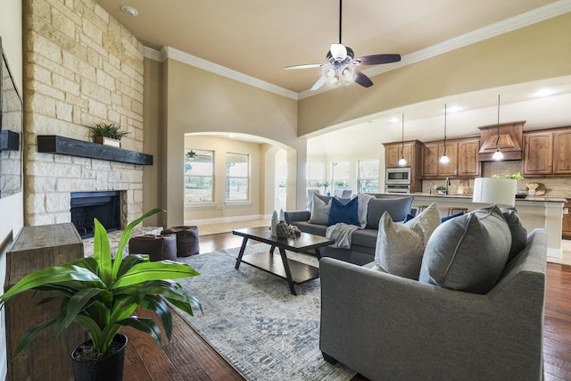 living room with ornamental molding, a stone fireplace, dark hardwood / wood-style floors, and ceiling fan