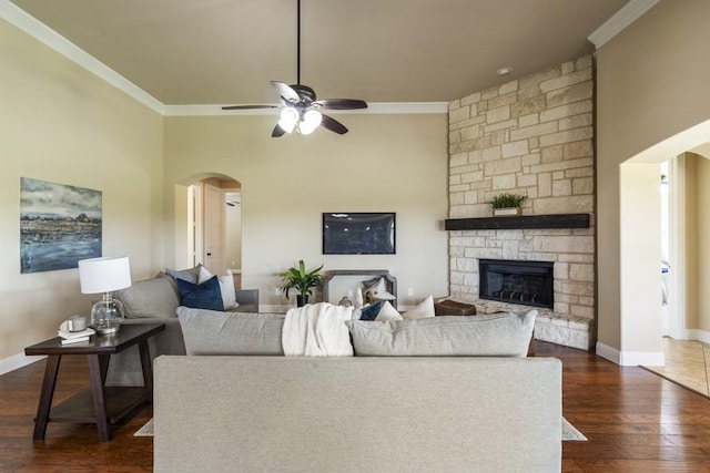 living room with dark wood-type flooring, ceiling fan, ornamental molding, and a stone fireplace