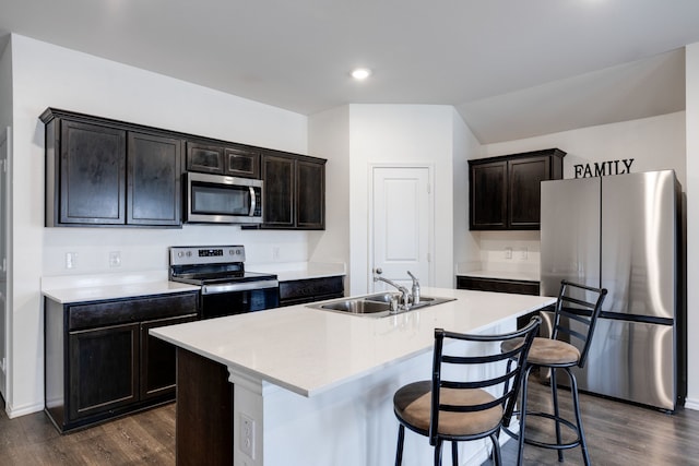 kitchen with sink, dark wood-type flooring, appliances with stainless steel finishes, a kitchen island with sink, and dark brown cabinetry