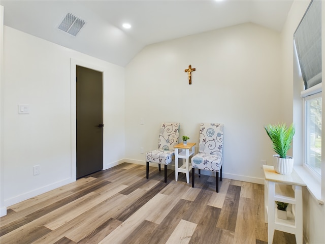 sitting room with lofted ceiling, visible vents, and wood finished floors