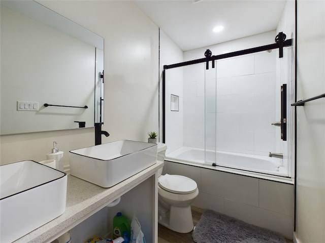 bathroom with combined bath / shower with glass door, a sink, toilet, and wood finished floors