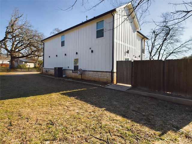 view of side of home with board and batten siding, central AC, fence, and a lawn