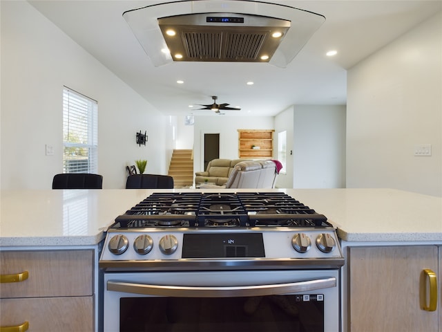 kitchen featuring stainless steel gas range oven, light stone counters, recessed lighting, open floor plan, and ventilation hood