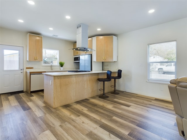 kitchen featuring island exhaust hood, stainless steel appliances, light countertops, light brown cabinets, and a peninsula