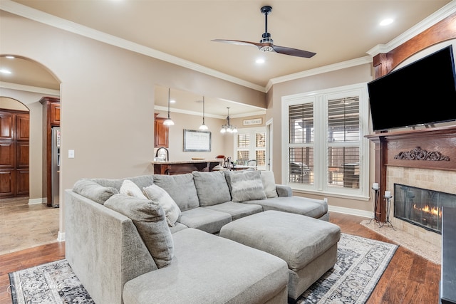 living room featuring ceiling fan, ornamental molding, a fireplace, and light hardwood / wood-style flooring