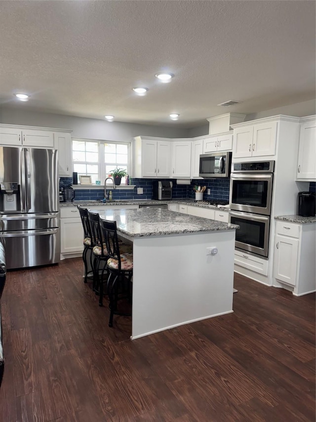 1006 High Point Dr, Mineral Wells, TX 76067 - kitchen with appliances with stainless steel finishes, a kitchen island, dark wood-style flooring, decorative backsplash, and a textured ceiling