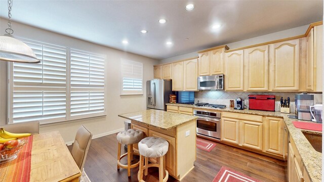 kitchen featuring tasteful backsplash, hanging light fixtures, light brown cabinets, appliances with stainless steel finishes, and light stone countertops