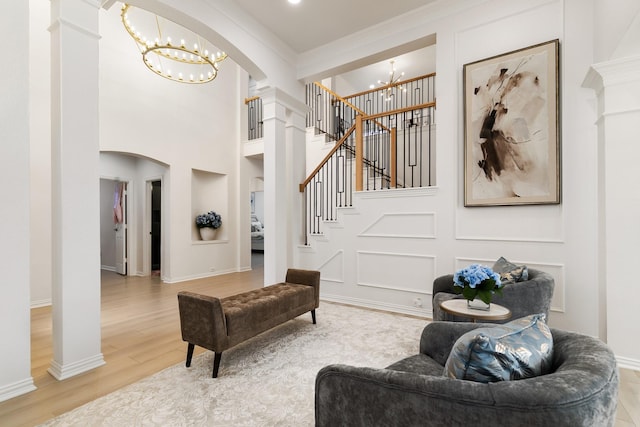 living room featuring a notable chandelier, wood-type flooring, ornamental molding, and ornate columns