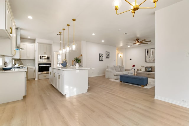 kitchen featuring light hardwood / wood-style flooring, a kitchen island with sink, hanging light fixtures, stainless steel appliances, and white cabinets