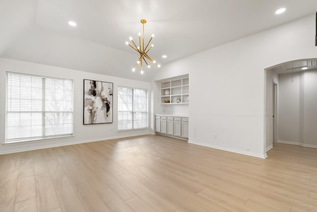 unfurnished living room featuring an inviting chandelier, lofted ceiling, built in shelves, and light hardwood / wood-style flooring