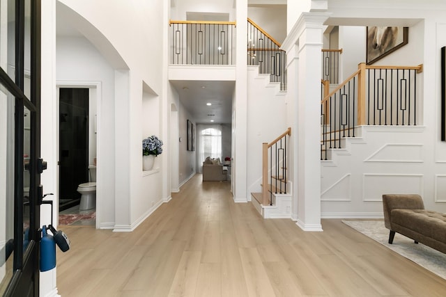 foyer featuring ornate columns, a towering ceiling, and light hardwood / wood-style flooring