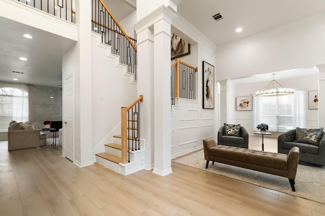 interior space with a notable chandelier, plenty of natural light, light hardwood / wood-style floors, and ornate columns