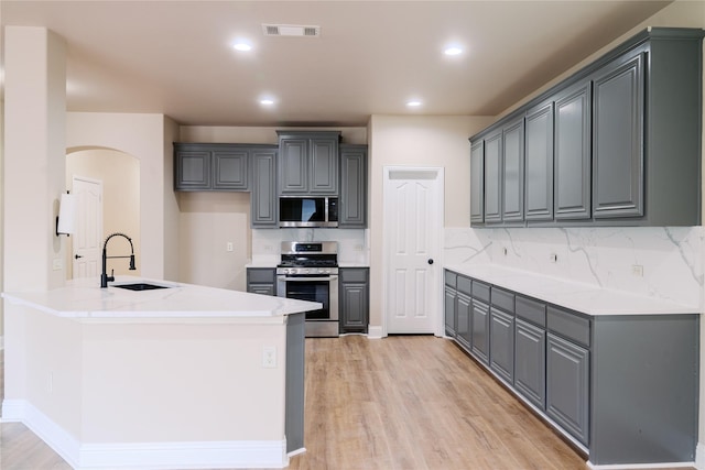 kitchen with sink, gray cabinetry, tasteful backsplash, light wood-type flooring, and stainless steel appliances