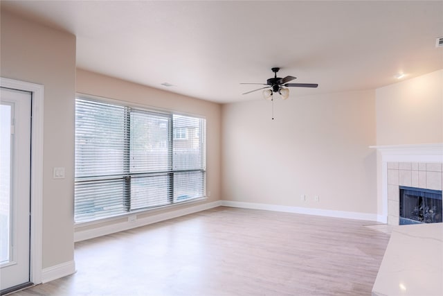 unfurnished living room with ceiling fan, a tiled fireplace, and light hardwood / wood-style floors