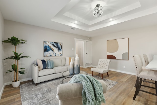 living room featuring an inviting chandelier, a tray ceiling, and light wood-type flooring