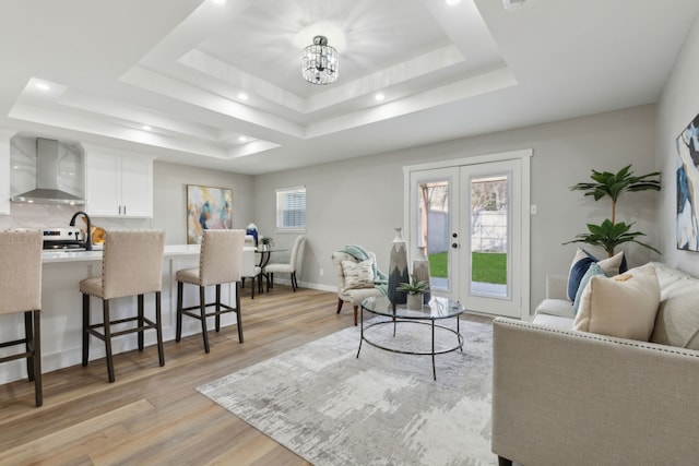 living room featuring french doors, a tray ceiling, a chandelier, and light hardwood / wood-style floors