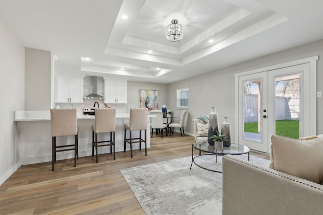 living room with a healthy amount of sunlight, a raised ceiling, and light hardwood / wood-style flooring