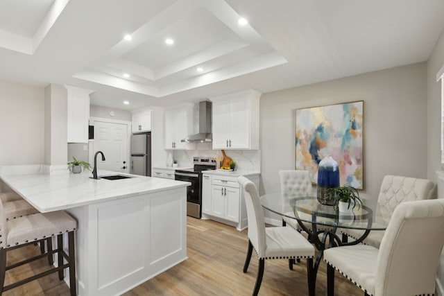 kitchen featuring sink, a breakfast bar area, appliances with stainless steel finishes, white cabinets, and wall chimney exhaust hood