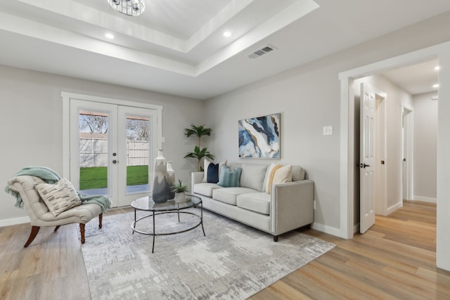 living room with a tray ceiling, light hardwood / wood-style floors, and french doors