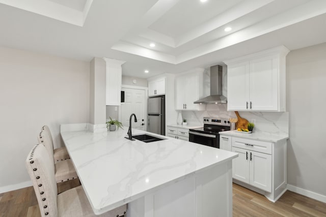 kitchen featuring sink, appliances with stainless steel finishes, white cabinetry, a kitchen bar, and wall chimney exhaust hood