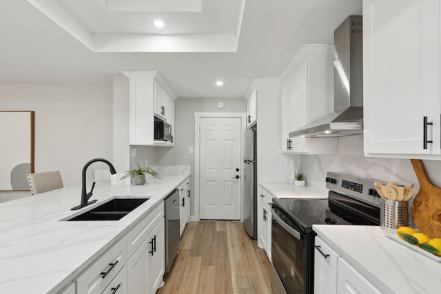 kitchen featuring wall chimney range hood, sink, white cabinetry, stainless steel appliances, and light stone countertops