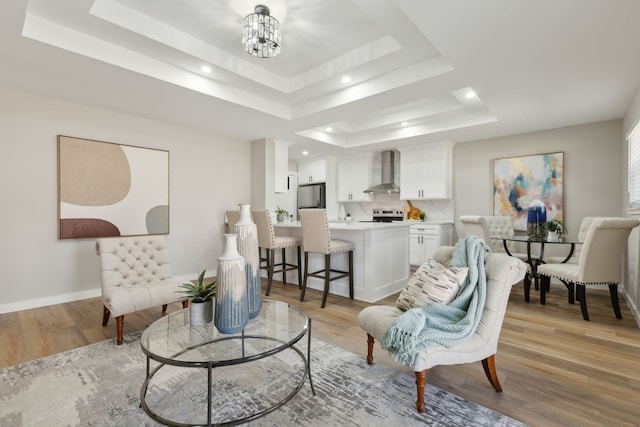 living room featuring a raised ceiling, a notable chandelier, and light hardwood / wood-style floors