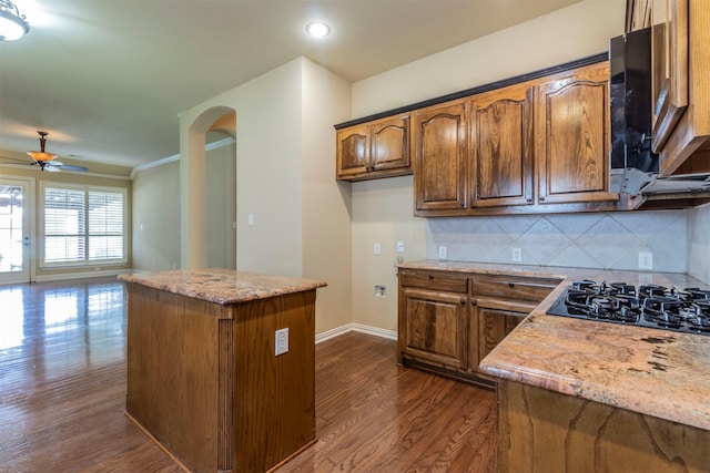 kitchen featuring black gas cooktop, dark hardwood / wood-style flooring, decorative backsplash, a center island, and light stone counters