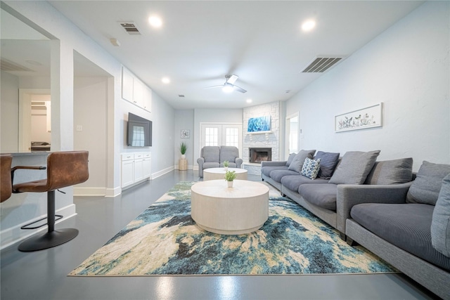 living room with a ceiling fan, a fireplace, visible vents, and concrete flooring